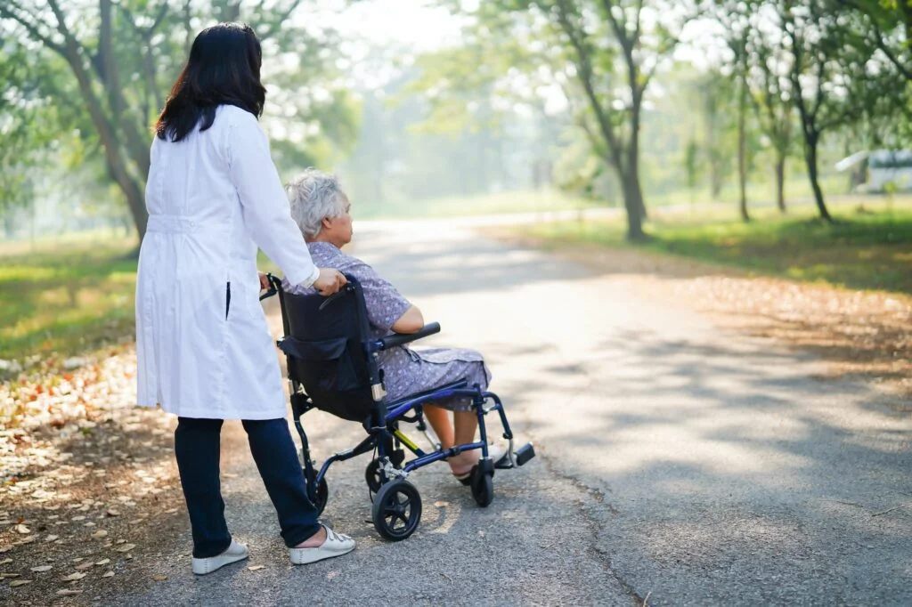 Doctor help and care Asian senior woman patient sitting on wheelchair at park.